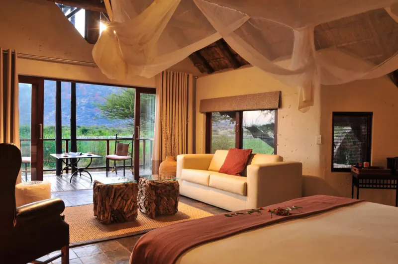 Luxurious lodge suite with yellow sofa, draped bed, balcony overlooking mountains and green valley at Tau Game Lodge.