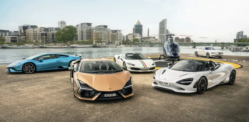 Luxury supercars: blue Lamborghini Huracan, gold Huracan STO, white McLaren 720S Spider parked by river with city skyline and helicopter.