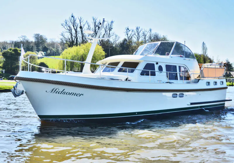 White motor cruiser 'Mahogany' cruising on river with trees and houses in background.