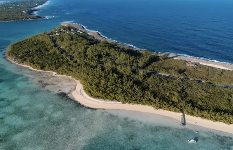Aerial view of lush green Lot 43 Bottom Harbour Beachfront property in the Bahamas, with white sand beach, turquoise waters, and a small boat.