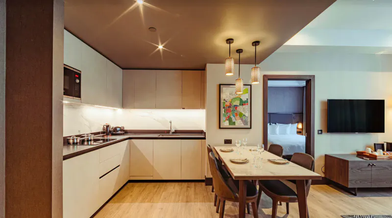 Modern luxury apartment kitchen and dining area with wooden table, chairs, pendant lights, and abstract wall art.