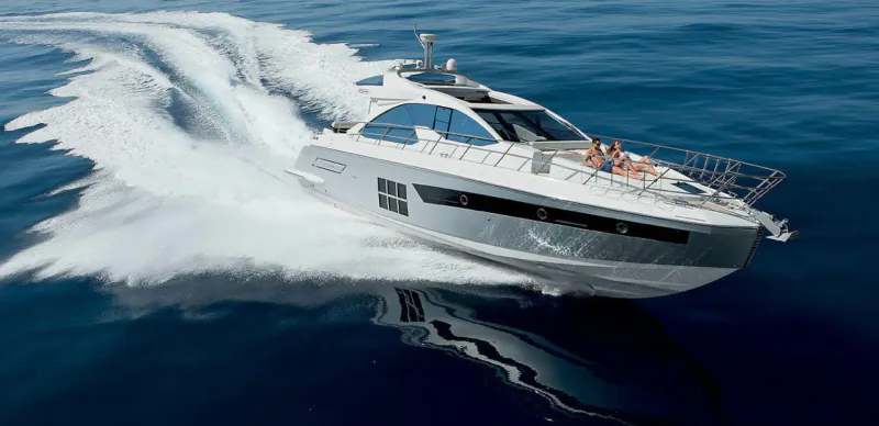 White luxury yacht speeding on blue ocean with passengers aboard, white wake trailing behind.
