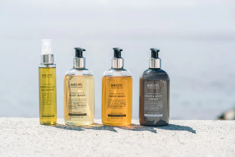 Elm Organics Norway body wash bottles in green oil, amber, and gray on seaside ledge