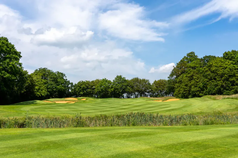 Wide view of Chart Hills golf course with manicured fairways, golden bunkers, lush trees, and blue sky.
