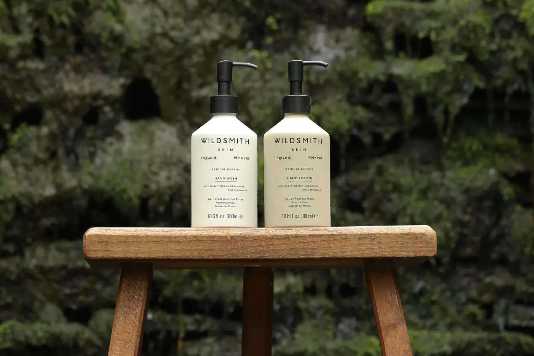 Two Wildsmith The Treehouse pump bottles on wooden stool in lush green forest setting.