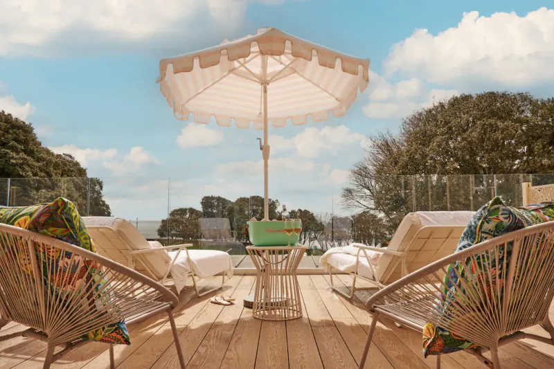 Stylish seaside deck in Bournemouth with cream fringed umbrella, green cooler, rattan lounge chairs with colorful cushions, ocean view