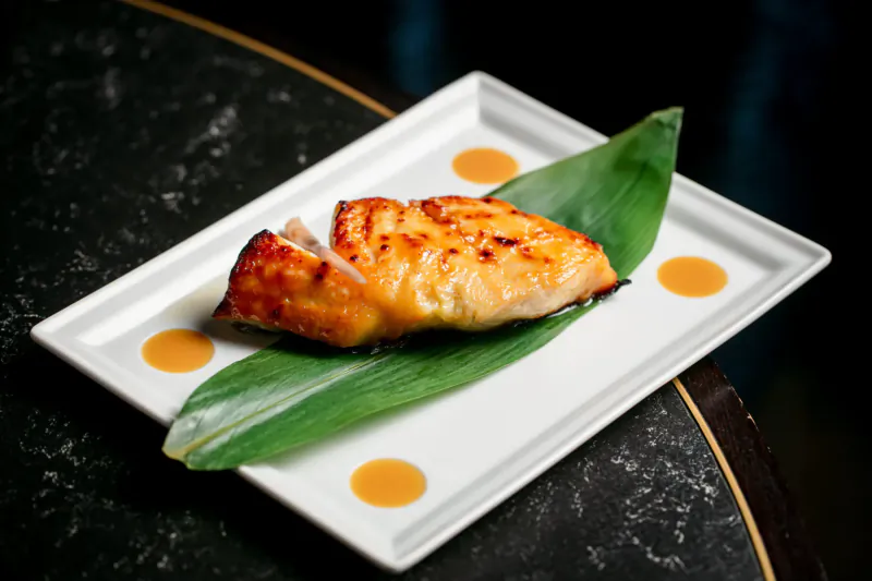 Grilled salmon fillet on perilla leaf, garnished with orange dots, on white plate at Nobu Hotel Marylebone.