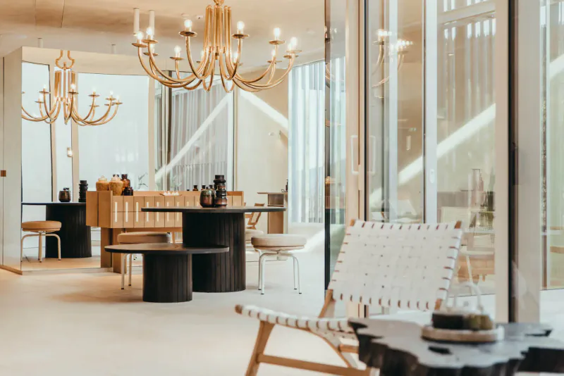 Elegant spa interior at Maslina Resort with multiple chandeliers, wooden tables, rattan chairs, and large windows