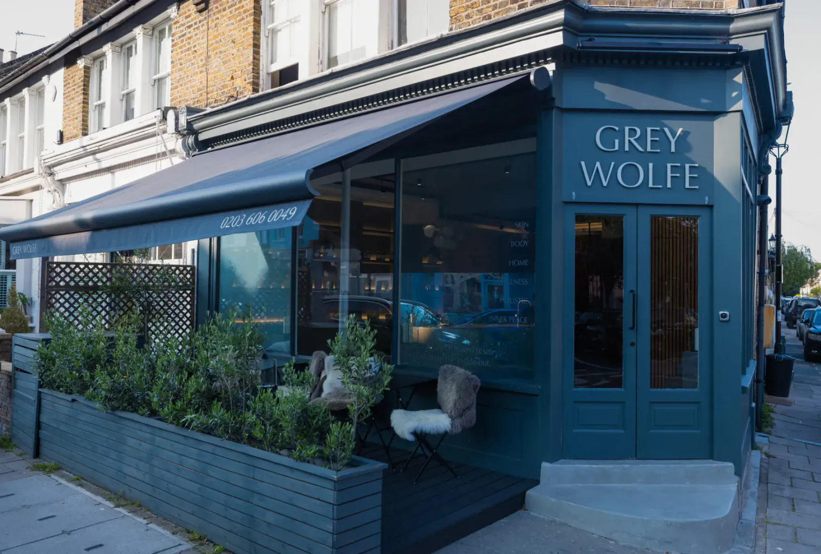 Grey Wolfe luxury wellness space on London street with grey awning, plants, chairs, and large signage.