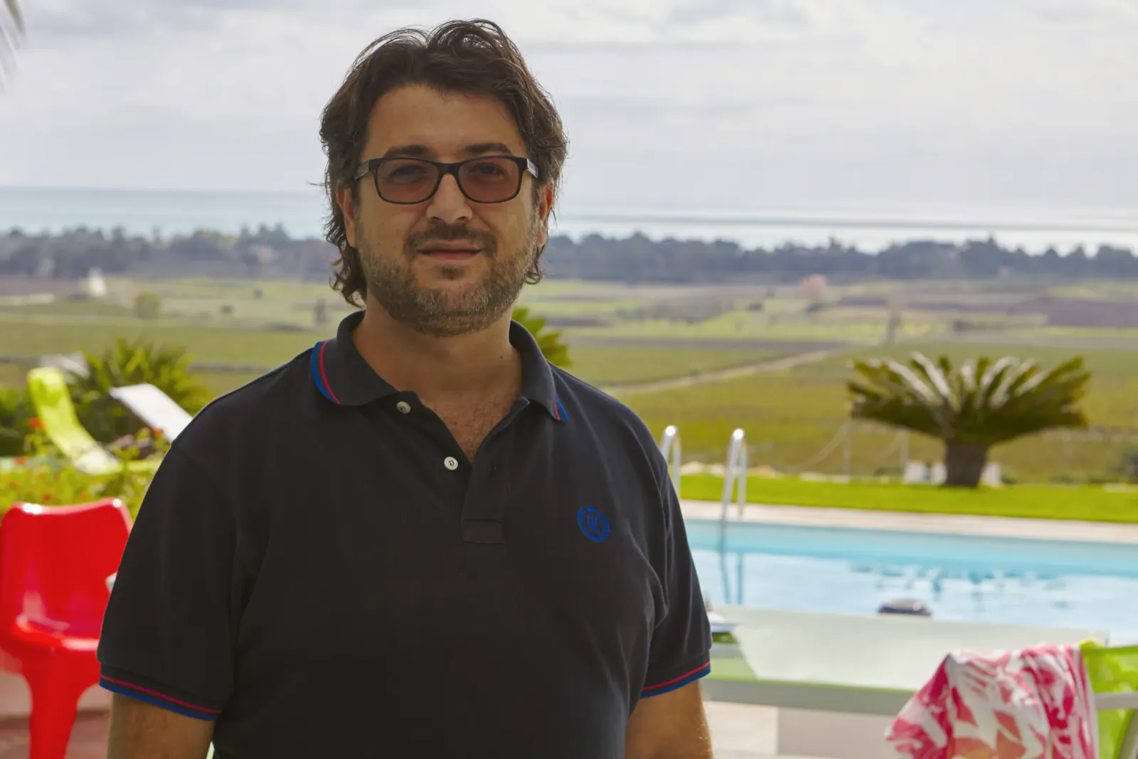 Gioacchino Sortino, Wish Sicily founder, smiling in black polo by pool overlooking vineyards and sea