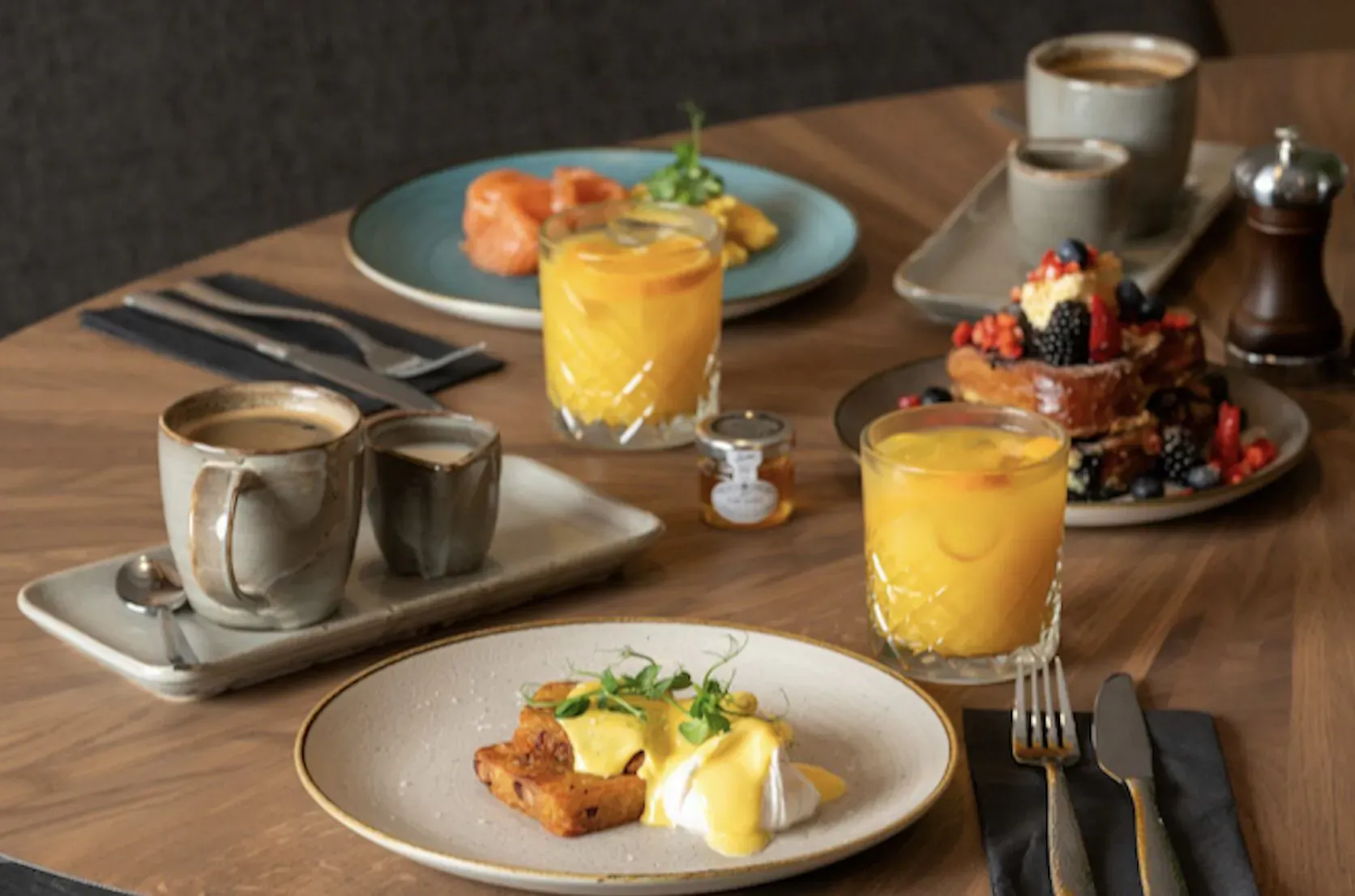 Wooden table with breakfast: eggs Benedict, French toast with berries, orange juice, coffee at The Reach hotel.