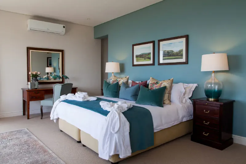 Luxurious bedroom at Tintswalo Boulders with king bed, teal pillows, vanity, and landscape art on teal walls.