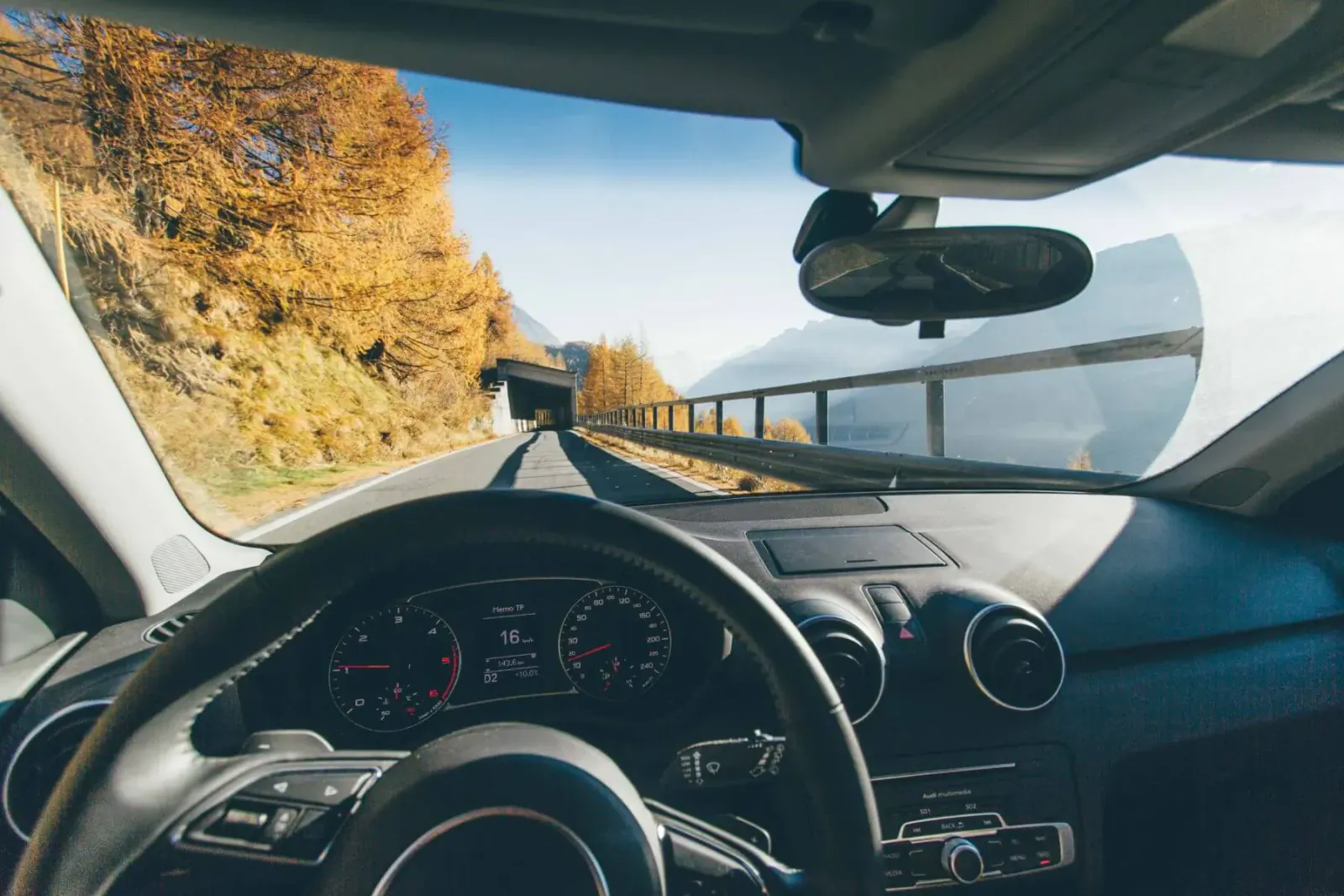 Dashboard view from luxury car driving on mountain road with autumn yellow trees and viaduct.