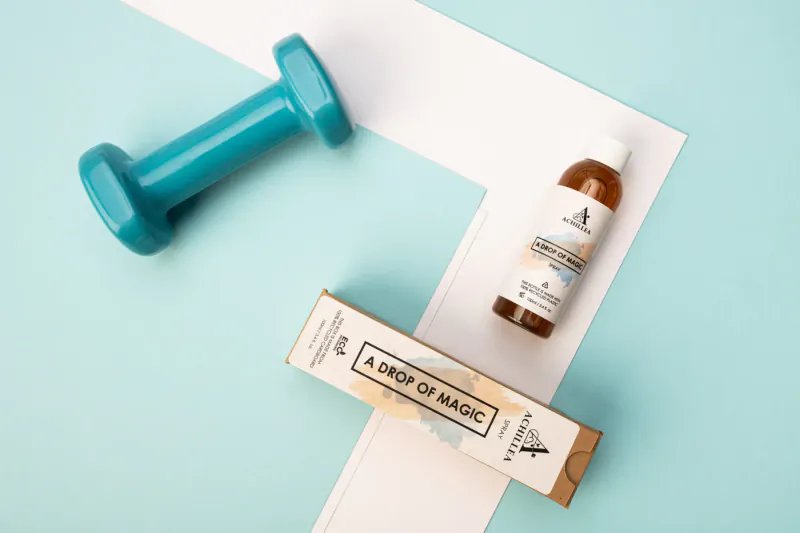Teal dumbbell beside 'A Drop of Magic' beauty product box and bottle on teal background