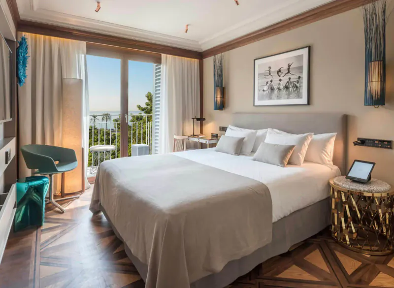 Elegant hotel room at El Llorenç Parc de la Mar with king bed, balcony view of sea and pines, modern decor.