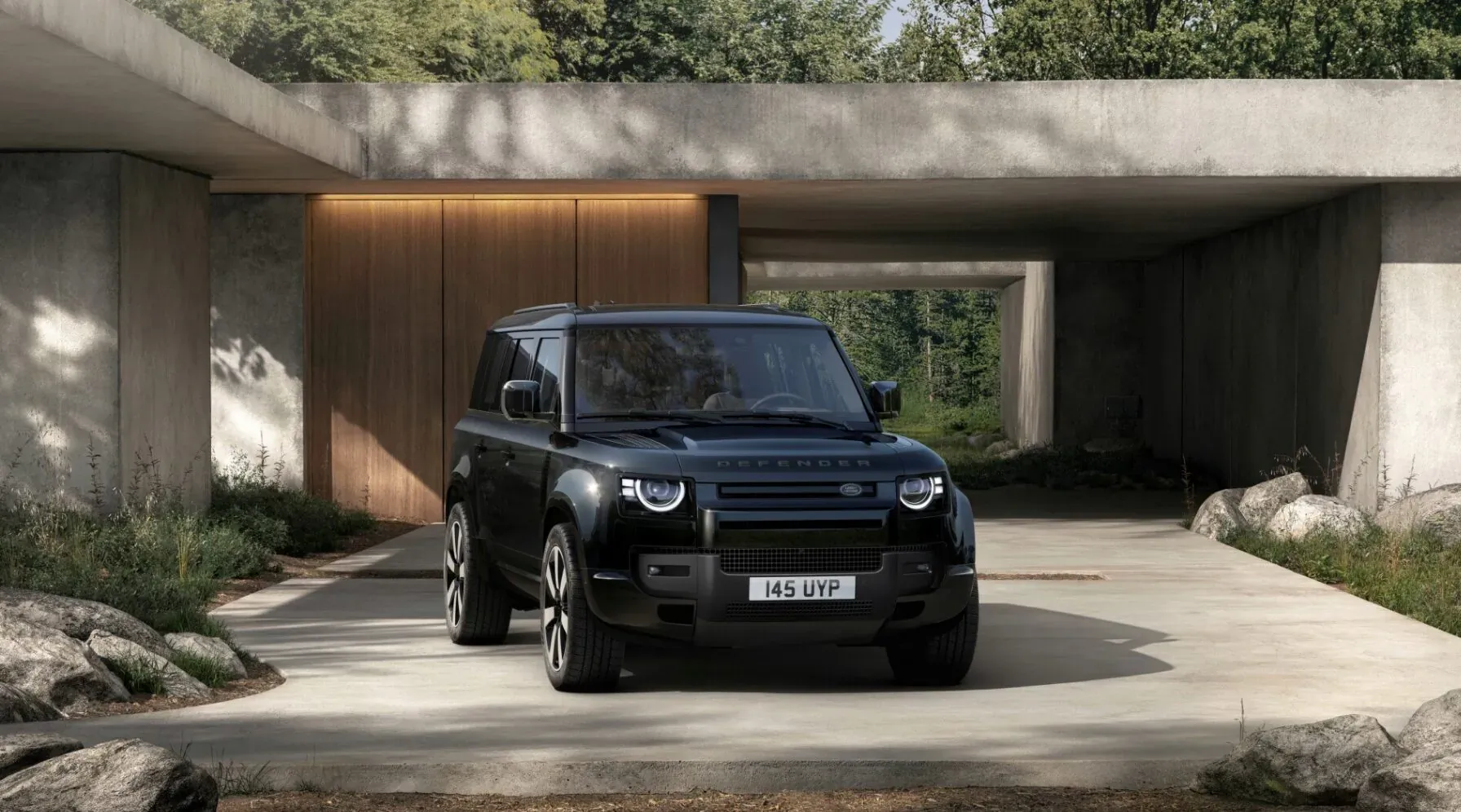 Black Land Rover Defender 4x4 parked in modern outdoor garage with concrete architecture and greenery