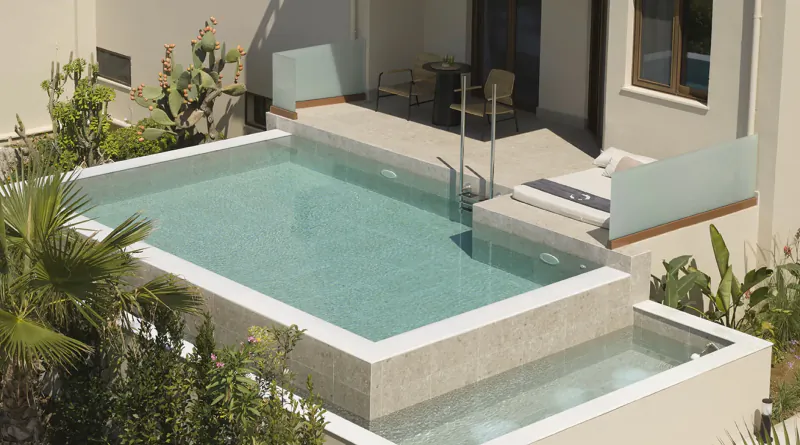 Aerial view of infinity pool at Asterion Suites & Spa, Crete, with turquoise water, lounge chairs, and tropical plants.