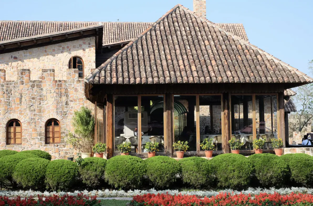 Luxury stone home with terracotta tile roof, wooden veranda, and landscaped gardens with red flowers