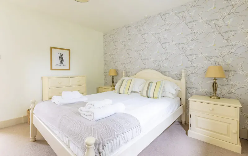 Cozy bedroom at Broomhill Manor with white wooden bed, crisp white linens, yellow pillows, matching nightstands, and lamps on grey floral wallpaper.