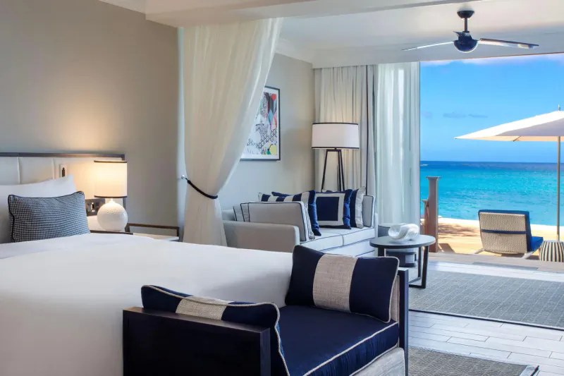 Luxurious Fairmont Royal Pavilion beachfront suite with king bed, seating, open doors to turquoise ocean.