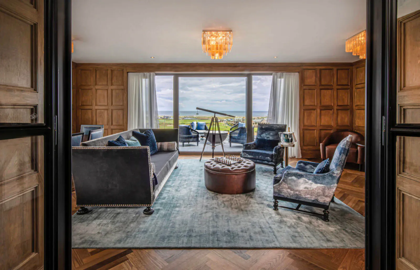 Elegant wood-panelled sitting room at Old Course Hotel with telescope, plush armchairs, sofa, and sea view balcony.