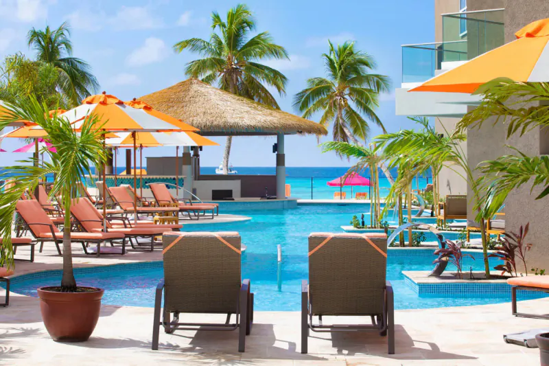 Luxury beach club poolside at O2 Beach Club & Spa, Barbados: orange umbrellas, loungers, palms, ocean view