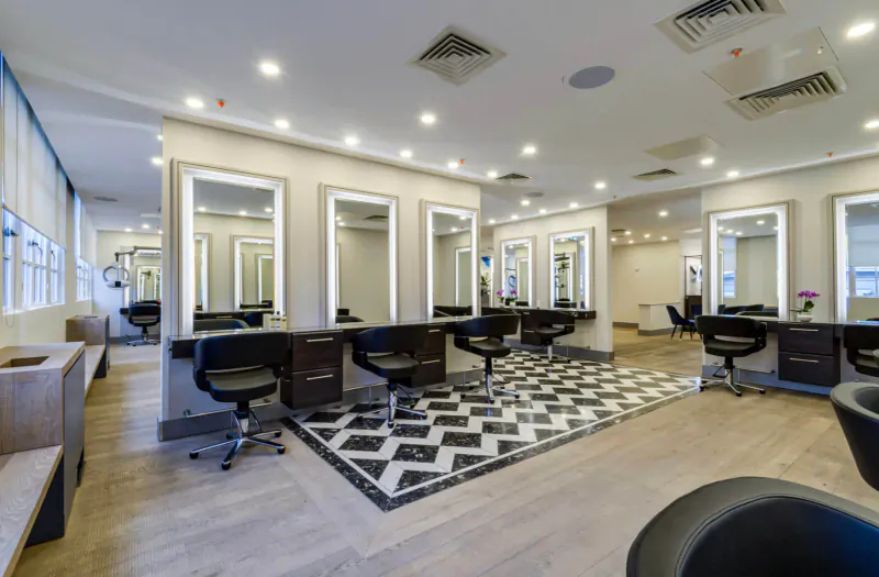 Modern Jo Hansford hairdressing salon with black styling chairs, lit mirrors, black-and-white checkered floor, and wooden accents.