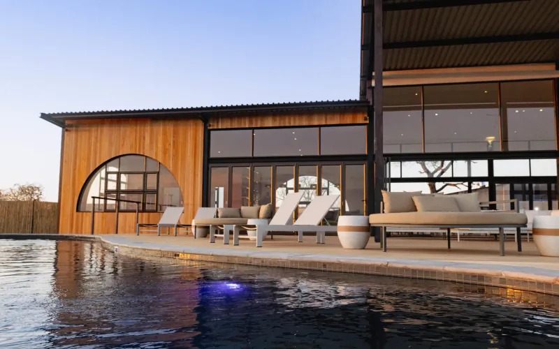 Modern wooden luxury house with curved windows, outdoor lounge seating by infinity pool at 18 On The Hill, Greater Kruger.