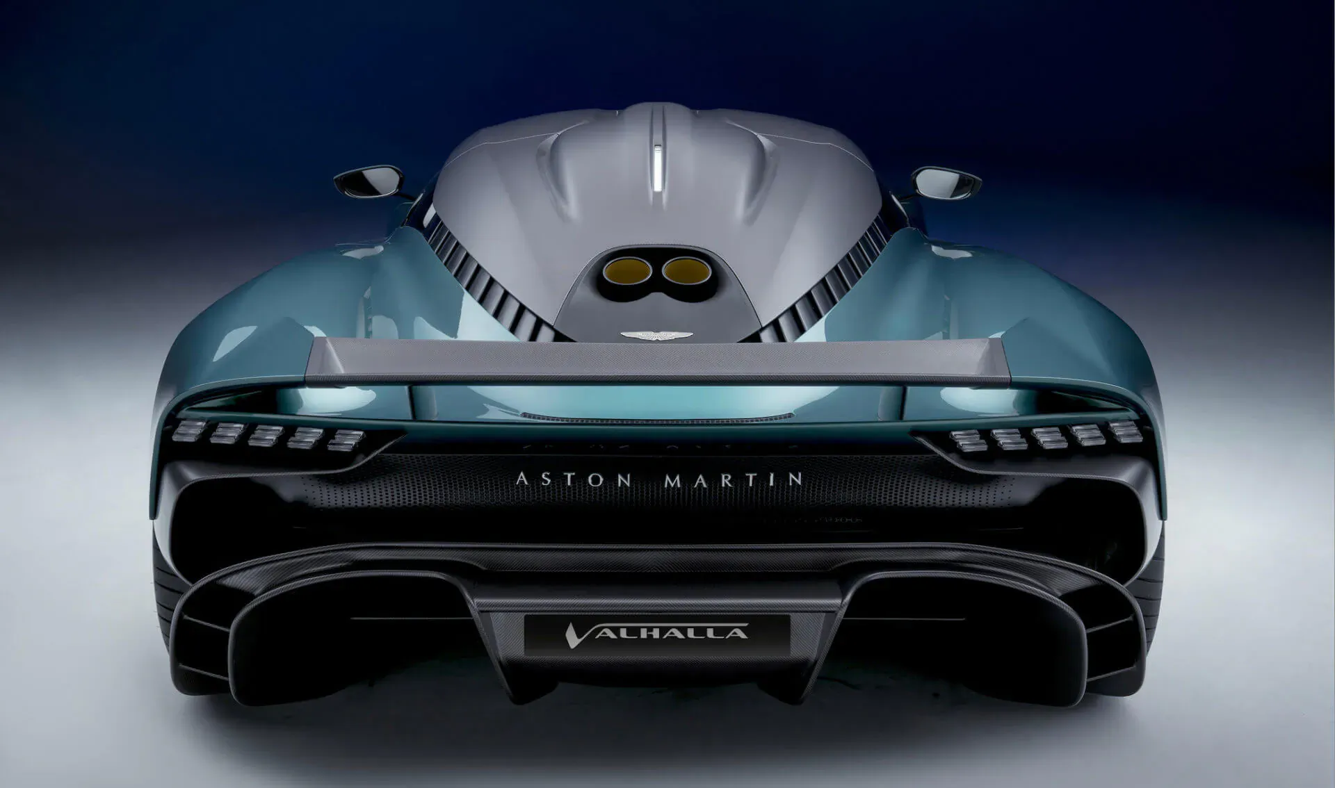 Rear view of teal Aston Martin Valhalla hybrid supercar with dual exhausts and Valkyrie badge on dark background.