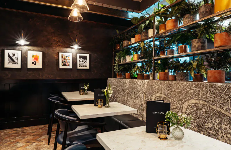 Six by Nico Canary Wharf gallery: elegant dining area with Ancient Rome decor, plants, pendant lights, art, and tables with menus.