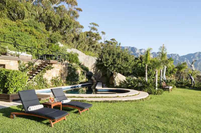 Luxury poolside lounge chairs and statue at 21 Nettleton, Clifton, Cape Town, with ocean views, lush gardens, and mountains.