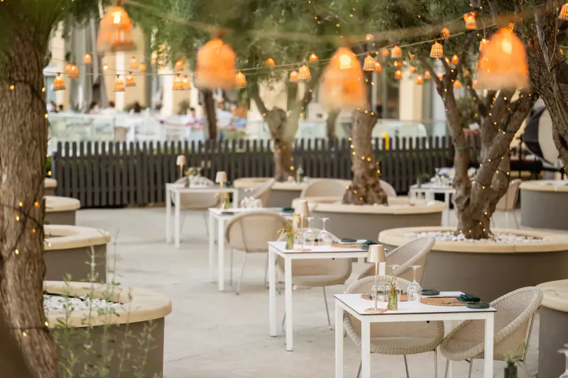 Outdoor terrace dining at Hilton Malta with white tables, chairs, olive trees, and hanging lanterns at night.