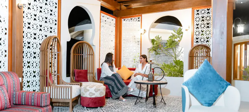Two women chatting on plush chairs around a small table in a luxurious Moroccan-style lounge at Hideaway Beach Resort.