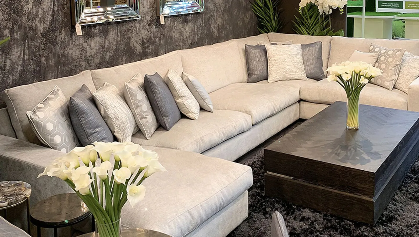 Luxury L-shaped beige sofa with gray pillows, white calla lilies, and dark wood coffee table in upscale living room