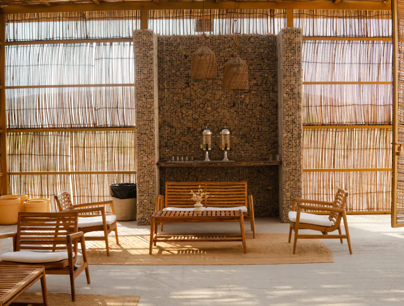 Luxurious desert lounge with bamboo walls, rattan furniture, cushioned bench, low table, and silver ice bucket on stone counter.