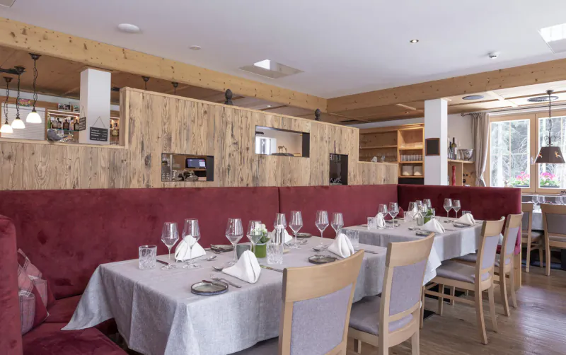 Elegant dining room in Hotel Kösslerhof with long white-clothed table, red velvet benches, wine glasses, and alpine window view.