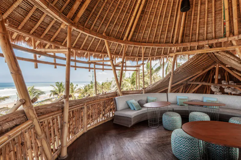 Bamboo beach club lounge in Bali with curved seating, ocean view, and tropical palms.