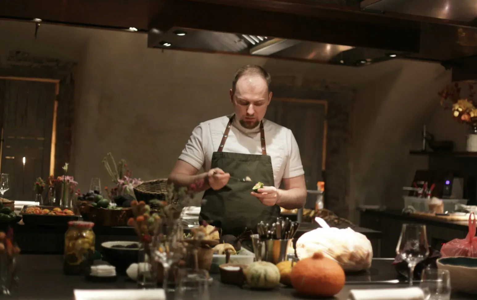 Bald man in white shirt and green apron preparing vegetables on counter in modern kitchen
