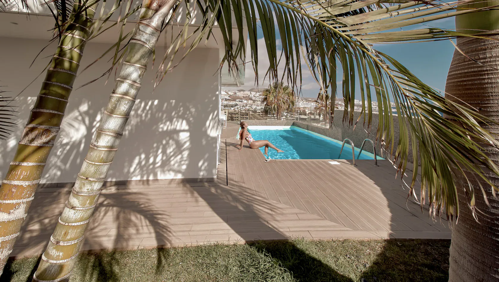 Woman sitting on edge of infinity pool at Baobab Suites resort in Tenerife, surrounded by palms and ocean view