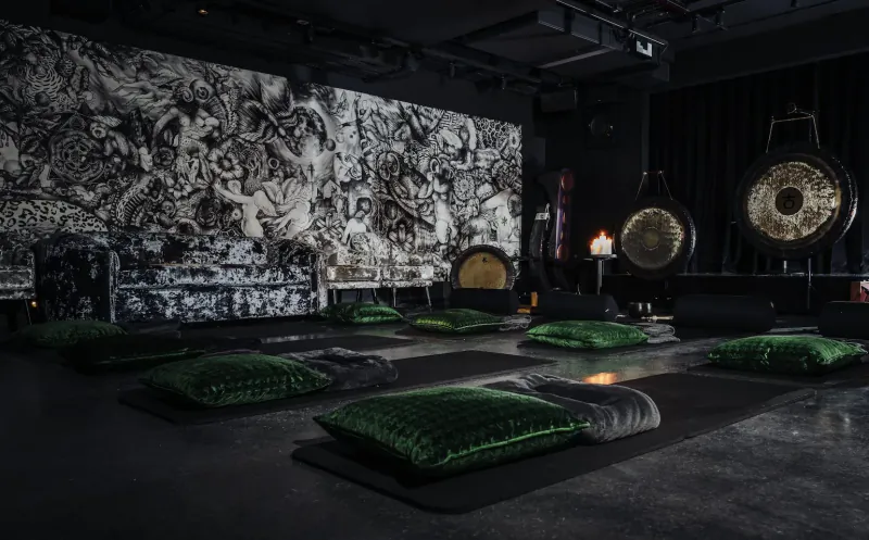 Zen room with green yoga mats and pillows, large gongs, candlelight, and intricate black-and-white wall mural at The Mandrake, London
