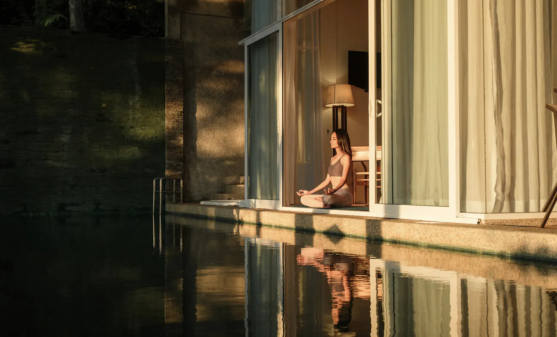 Woman meditating in lotus pose on deck by pool at sunset, yoga retreat overlooking water, Ambong-Ambong Langkawi