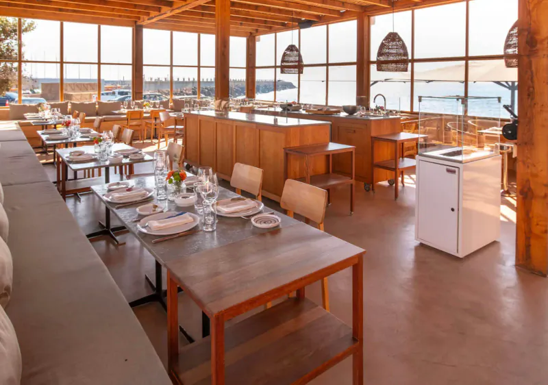 Spacious wooden Gastro Beach restaurant in Palma with tables set for dining, open kitchen, and sea views through large windows.