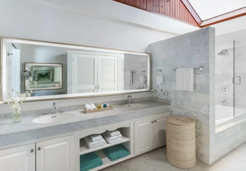 Luxurious bathroom at Spice Island Beach Resort with double vanity, large mirror, glass shower, and wicker basket.