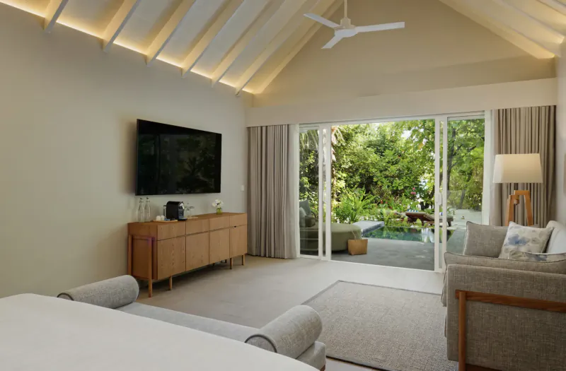 Luxurious Amari Raaya Maldives villa bedroom with plush bed, TV, sofa, and sliding doors to lush garden pool.