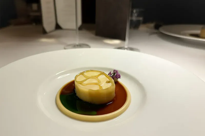 Close-up of Saint Pierre dish: cylindrical garlic on green sauce ring with purple flower, on white plate