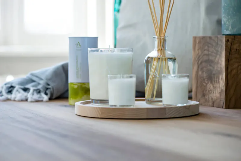 Arranged Arran spring home fragrance: reed diffuser, candles, and essential oil on wooden tray with blocks and towel.