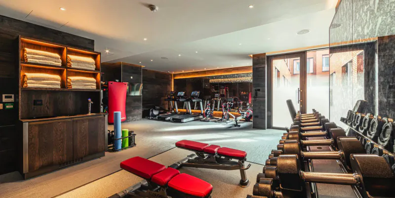 Spacious modern gym in luxury apartment with treadmills, weight benches, red mats, yoga balls, and towels on dark wood shelves.