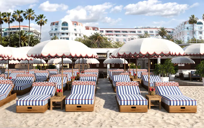 Luxury beachside lounge at Ciro’s, Hôtel Barrière Le Majestic Cannes: rows of white umbrellas and blue-striped loungers on sand with palm trees.