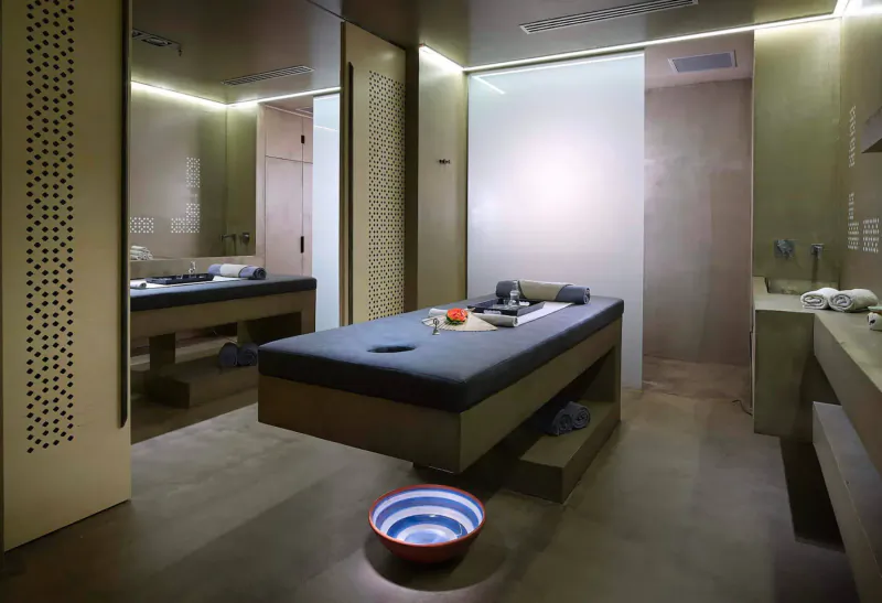 Modern spa room at Elysium Boutique Hotel Crete with massage table, towels, orange slices, and frosted glass shower.