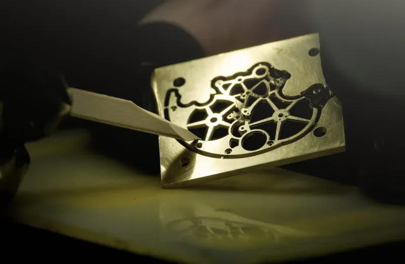 Close-up of intricate gold BOVET watch movement being cleaned with white tool on yellow surface